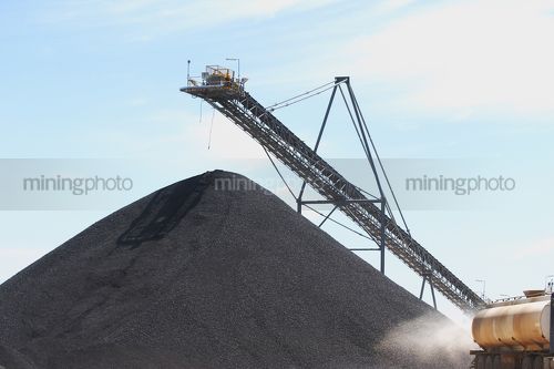 Water cart spraying water wioth coal stockpile and loader in background. - Mining Photo Stock Library