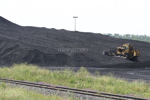 Bulldozer stockpiliong coal with rail lines in foreground.  green environment rehabilition in foreground. - Mining Photo Stock Library