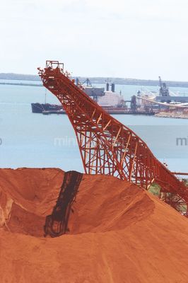 Bauxite stockpile with loader and ship wharf in background. - Mining Photo Stock Library