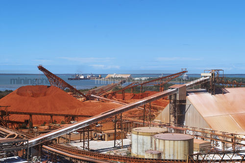 Bauxite stockpiles at alumina proecssing plant.  shipping and wharves in background. - Mining Photo Stock Library