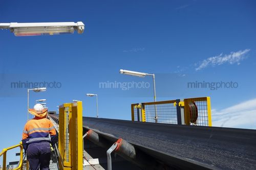 Mine worker on walkway next to coal conveyor.  shot from behind. - Mining Photo Stock Library