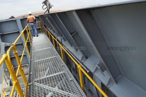 Mine worker standing on coal hopper observing stockpiled coal being loaded. - Mining Photo Stock Library