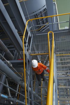 Mine site worker in full ppe safely using stairs in a processing plant.  shot from above - Mining Photo Stock Library