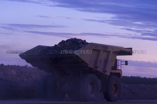 Haul truck carrying overburden travelling through open cut coal mine at twilight. - Mining Photo Stock Library