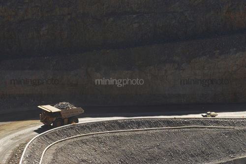 Light vehicle following loaded haul truck out of open cut mine. - Mining Photo Stock Library