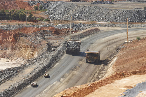 Loaded haul truck passes empty truck on circuit at open cut gold mine. light vehicles follow. - Mining Photo Stock Library