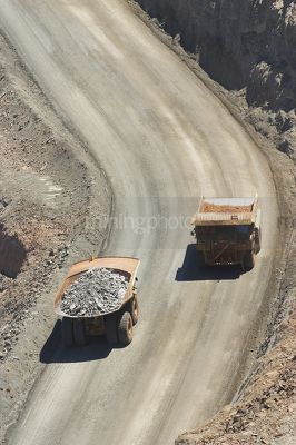Aerial, vertical shot of loaded haul trucks passing on gold haul road. - Mining Photo Stock Library