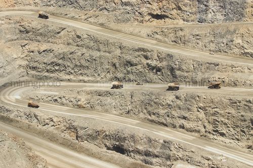 Many haul trucks loaded and empty weaving their way up steep haul road on way out of open cut gold mine. - Mining Photo Stock Library