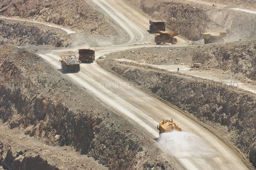 Water cart spraying water oin haul road with loaded and empty haul trucks n background. - Mining Photo Stock Library