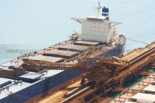 Iron ore ship loader working at terminal.  shot shows ship receiving iron ore into hold.  aerial photo. - Mining Photo Stock Library
