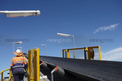 Mine worker in full PPE on walkway adjacent to new coal conveyor - Mining Photo Stock Library