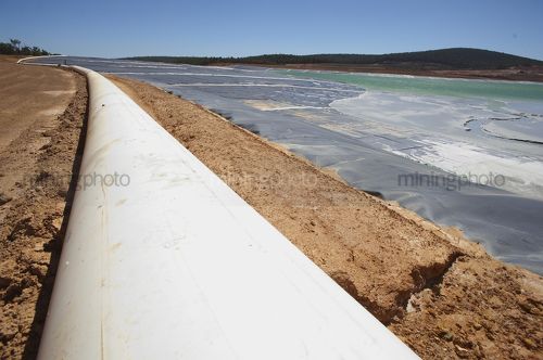 Outlet pipe leading to a large, lined, gold mine tailings dam. - Mining Photo Stock Library