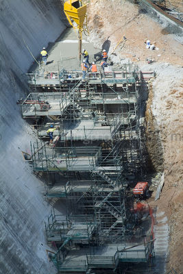Construction workers in full PPE working on scaffold and pouring concrete at dam build. - Mining Photo Stock Library