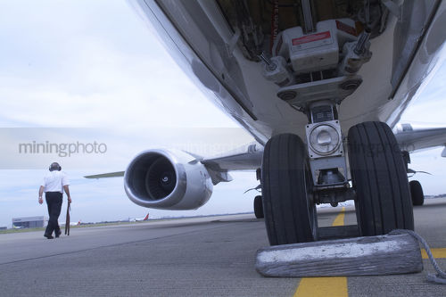 Pilot with ear protection does pre flight inspection of 747 plane at city airport.  shot from under the plane at tarmac level. - Mining Photo Stock Library