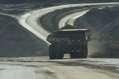 Loaded haul truck moving on haul road in open cut mine. dark exposure to capture flashing LED green lights on front to show its loaded. - Mining Photo Stock Library
