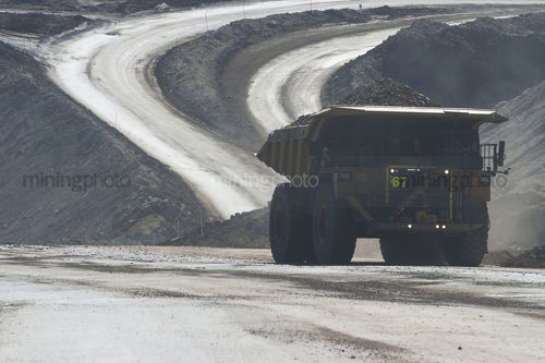 Loaded haul truck moving on haul road in open cut mine. dark exposure to capture flashing LED green lights on front to show its loaded. - Mining Photo Stock Library
