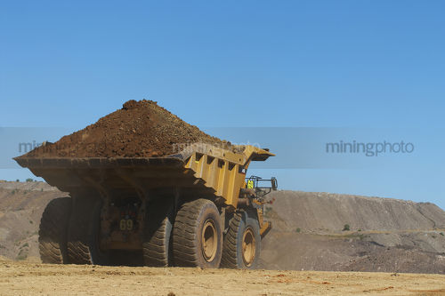Loaded haul truck with overburden heads to stockpile in open cut mine.  clear blue sky with plenty of space for copy. - Mining Photo Stock Library