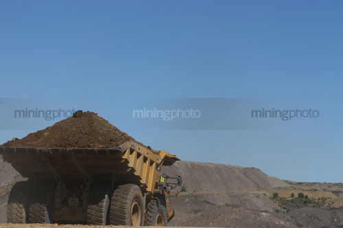 Loaded haul truck with overburden heads to stockpile in open cut mine.  clear blue sky with plenty of space for copy. - Mining Photo Stock Library