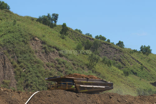 Loaded haul truck moving on haul access road with revegetated embankment behind. - Mining Photo Stock Library