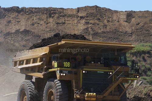 Loaded haul truck in open cut mine carrying over burden with high stockpiles behind. - Mining Photo Stock Library