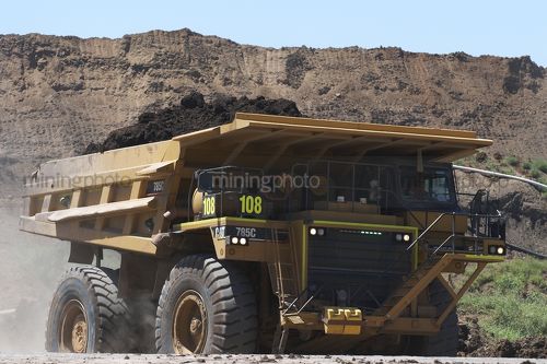 Loaded haul truck in open cut mine carrying over burden with high stockpiles behind. - Mining Photo Stock Library