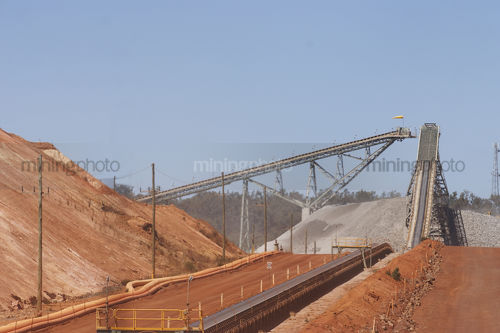 Haul road in open cut gold mine with conveyor leading to two stackers and large stockpile. - Mining Photo Stock Library