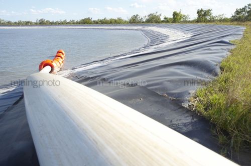 Tailings dam with rubber lining.  pipe entering from foreground and orange floats in water. - Mining Photo Stock Library
