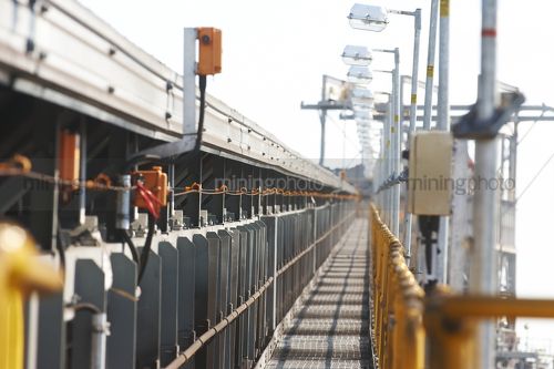 Long lens shot looking along walkway of covered coal conveyor on open cut mine.  emergency stop cord clearly visible and lighting towers. - Mining Photo Stock Library