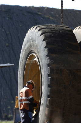 Tyre fitter mine worker inspecting haul truck tyre.  great scale.  vertical image. - Mining Photo Stock Library