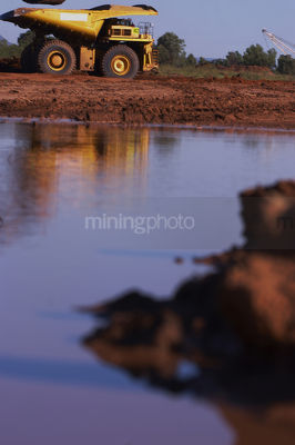 Afternoon light reflected on water with haul truck moving in background.  vertical shot. - Mining Photo Stock Library