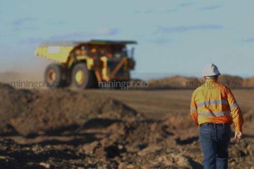 Mine worker in full PPE walking towards haul truck in open cut coal mine. - Mining Photo Stock Library