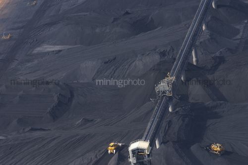Close up aerial photo of tractors stockpiling coal at shipping terminal.  conveyor working above to spread coal. - Mining Photo Stock Library