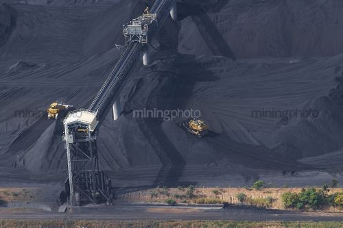 Close up aerial photo of tractors stockpiling coal at shipping terminal.  conveyor working above to spread coal. - Mining Photo Stock Library