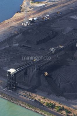 Vertical aerial photo of tractors stockpiling coal at shipping terminal.  conveyor working above to spread coal. - Mining Photo Stock Library