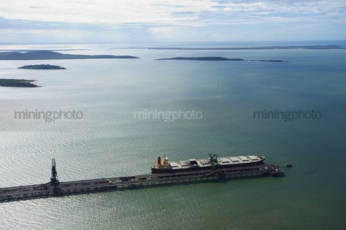 Wide aerial shot of coal ship being loaded at wharf.  lots of islands in background - Mining Photo Stock Library