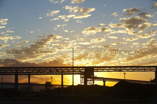 Sunset with stockpiled coal in foreground and high conveyors at terminal. - Mining Photo Stock Library