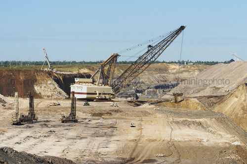 Dragline working in open cut mine with drill blasting rigs in foreground drilling. cranes, bulldozers and light vehicle show scale. - Mining Photo Stock Library