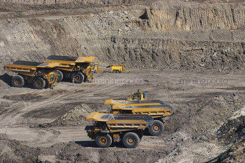 4 four haul trucks parked at go line in open cut coal mine.  worker in full PPE gives scale of machines.   - Mining Photo Stock Library