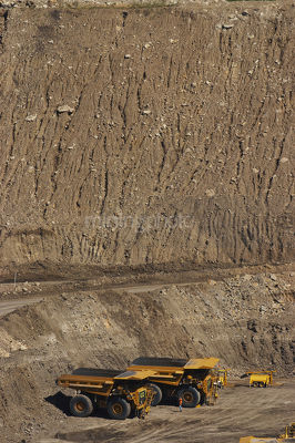 Vertical photo 4 four haul trucks parked at go line in open cut coal mine.  worker in full PPE gives scale of machines.   - Mining Photo Stock Library