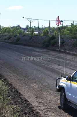 Vertical photo of light vehicle with flag parked on graded haul access road.  great shot of good haul road.  coal stockpile conveyor in background. - Mining Photo Stock Library