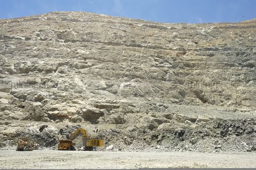 Really wide shot at ground level of deep open cut mine.  excavator loading haul truck and dozer standing by.  high walls of pit stretch up to blue sky.  great wide photo for two, double page spread or placement of copy. - Mining Photo Stock Library