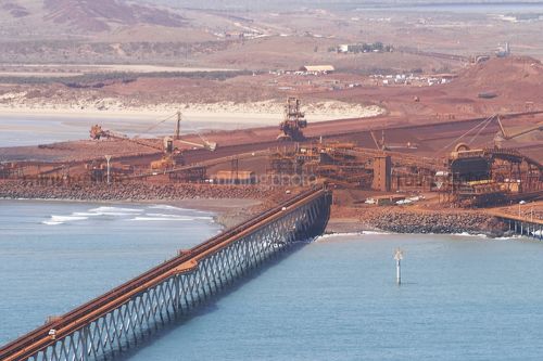 Aerial photo of iron ore shipping terminal.  light vehicle driving on wharf for scale with ore conveyors and ore loaders in background.  set right on ocean. - Mining Photo Stock Library