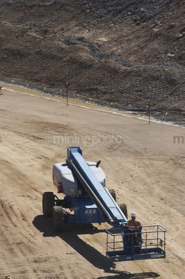 Vertical photo of worker in full PPE operating an EWP, Elevated Work Platform.  area worked is inside flagged, roped boundary. - Mining Photo Stock Library