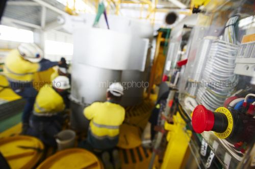 Emergency red stop button in focus with workers in background wearing full yellow PPE.  workers are out of focus. - Mining Photo Stock Library