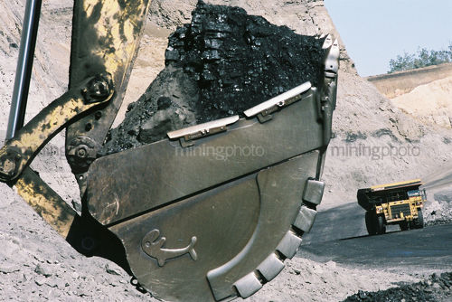 Close up shot of coal in an excavator bucket with haul truck on road in background.  open cut coal mining. - Mining Photo Stock Library