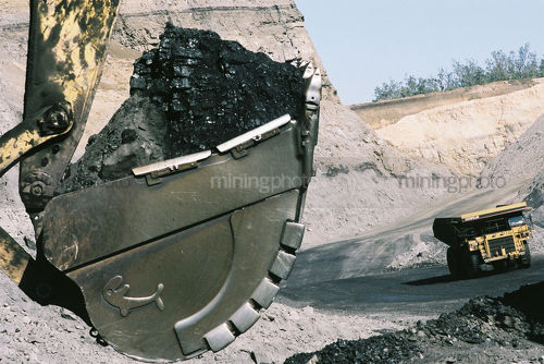Close up shot of coal in an excavator bucket with haul truck on road in background.  open cut coal mining. - Mining Photo Stock Library