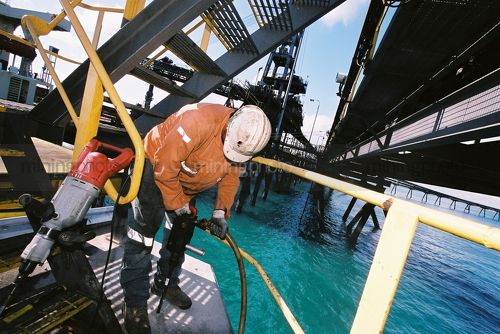 Marine worker on scaffolding steps at shipping wharf.  shot at water level with ship wharf in background. - Mining Photo Stock Library