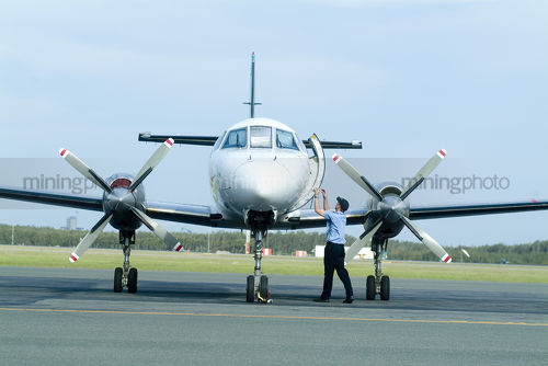 Young male pilot closing door on propeller twin engine plane on tarmac - Mining Photo Stock Library