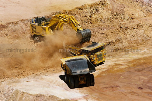 Close up photo of excavator loading overburden into haul truck. - Mining Photo Stock Library