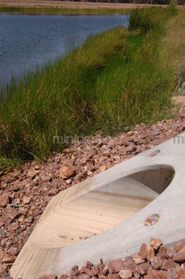 Vertical image of a concrete culvert pipe outlet into planted water storage dam on mine site. - Mining Photo Stock Library